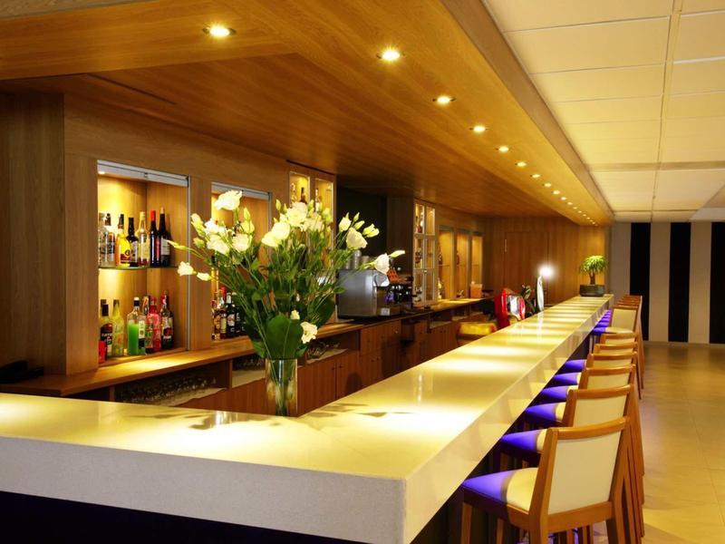 Moderní hotelový bar s bílým pultem, barovými stoličkami a květinovou výzdobou.