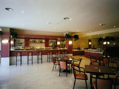 Leerer Barraum mit großen Tischen, Holzstühlen und langer Theke mit Barhockern bei hellem Licht.