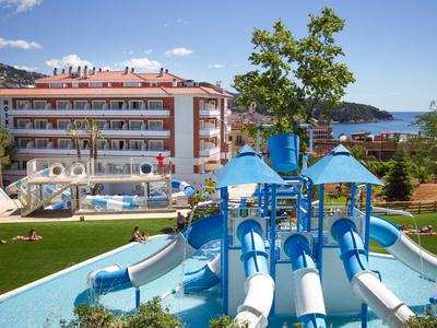 Bunter Wasserspielplatz mit Rutschen vor einem Hotel mit Pool und Bergblick.