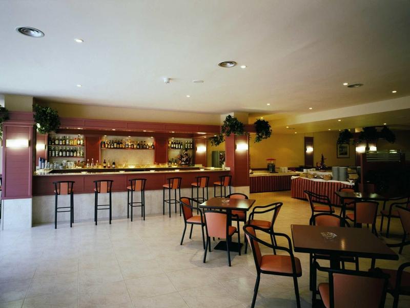 Leerer Barraum mit großen Tischen, Holzstühlen und langer Theke mit Barhockern bei hellem Licht.