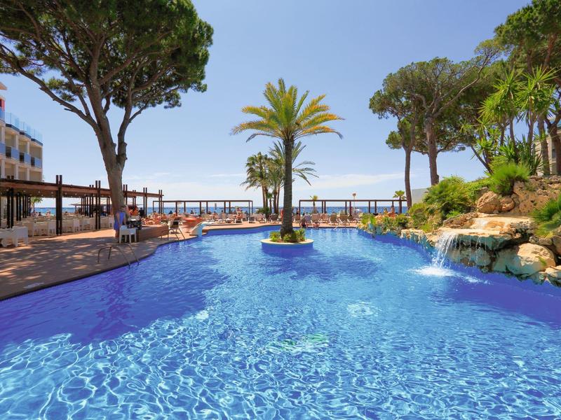 Blue pool with palm trees and lounge chairs under blue sky at a resort.