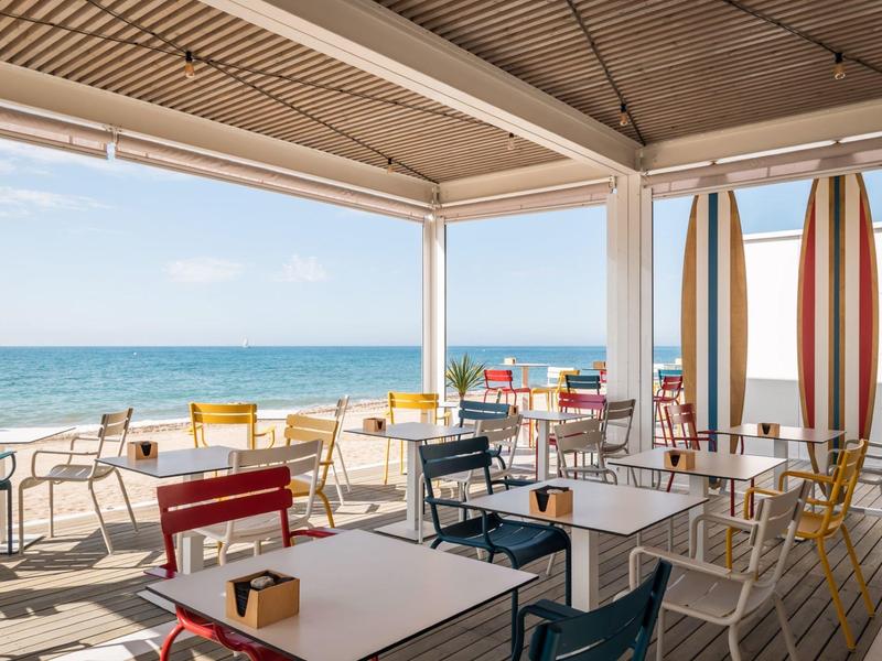 Outdoor terrace with tables and colorful chairs overlooking the ocean and blue sky.
