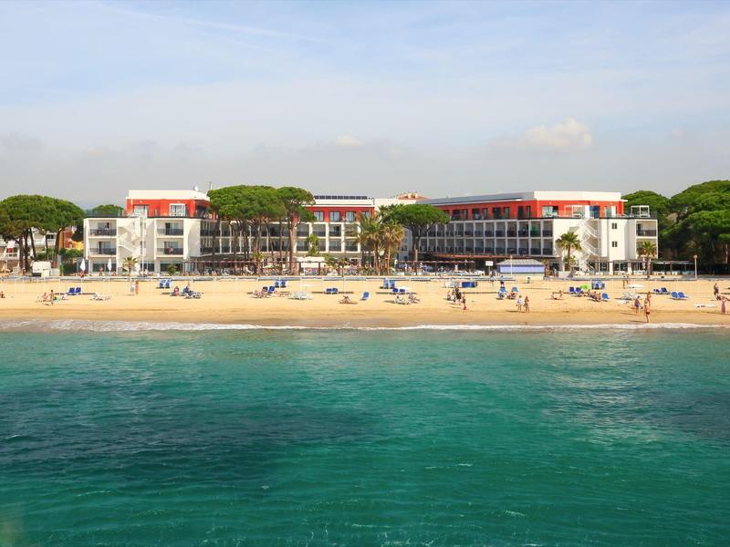 Beachfront hotel with sunbathers on sandy beach and calm turquoise sea under clear sky.