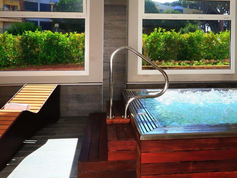 Modern indoor jacuzzi with wooden loungers and large windows overlooking greenery.