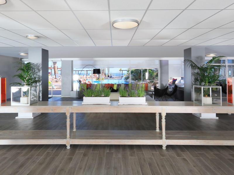 Modern hotel lobby with white tables, greenery, and seating area by large windows.