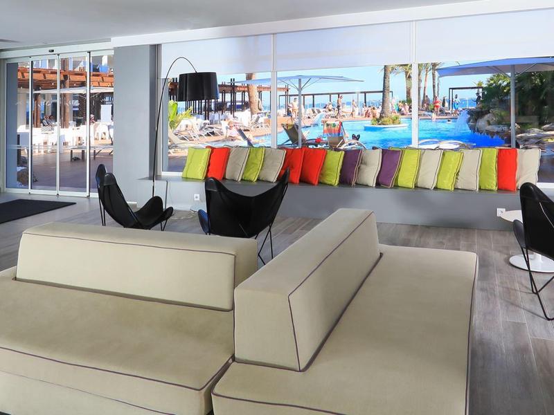 Modern hotel lounge with beige sectional sofa, black chairs, colorful pillows, and large windows.