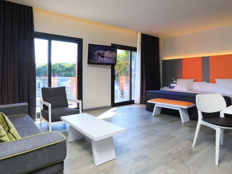 Modern hotel room with a large bed, desk, sofa, and balcony with scenic view.