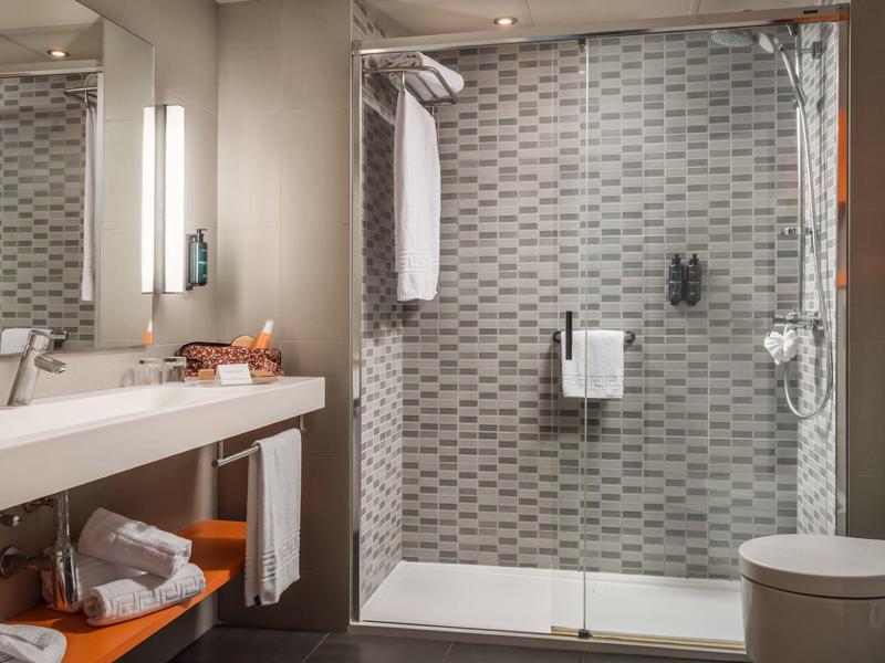 Modern bathroom with glass shower enclosure, patterned tiles, white sink, and wooden shelves.