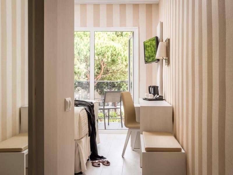 Compact hotel room with striped walls, small desk, chair, bed, and balcony view.
