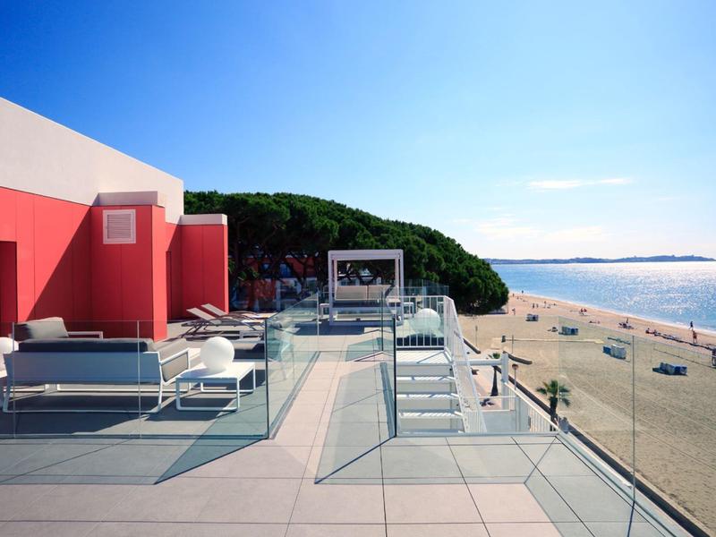 Spacious terrace with modern furniture overlooking a sunny beach and ocean.