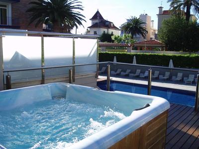 Whirlpool mit sprudelndem Wasser auf Holzterrasse, dahinter blauer Pool und Palmen.