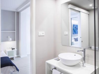 Helles Badezimmer mit rundem Waschbecken, großem Spiegel und Blick ins Schlafzimmer, weiße Wände.