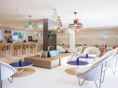 Heller, moderner Lounge-Bereich mit weißen Stühlen, blauem Dekor und Holztischen in offenem Raum.