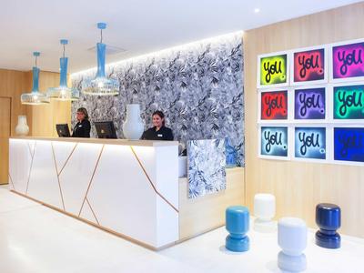 Helle Empfangshalle mit weißen Theken, blauer Wandgestaltung, modernen Hockern und farbigen Wandbildern.