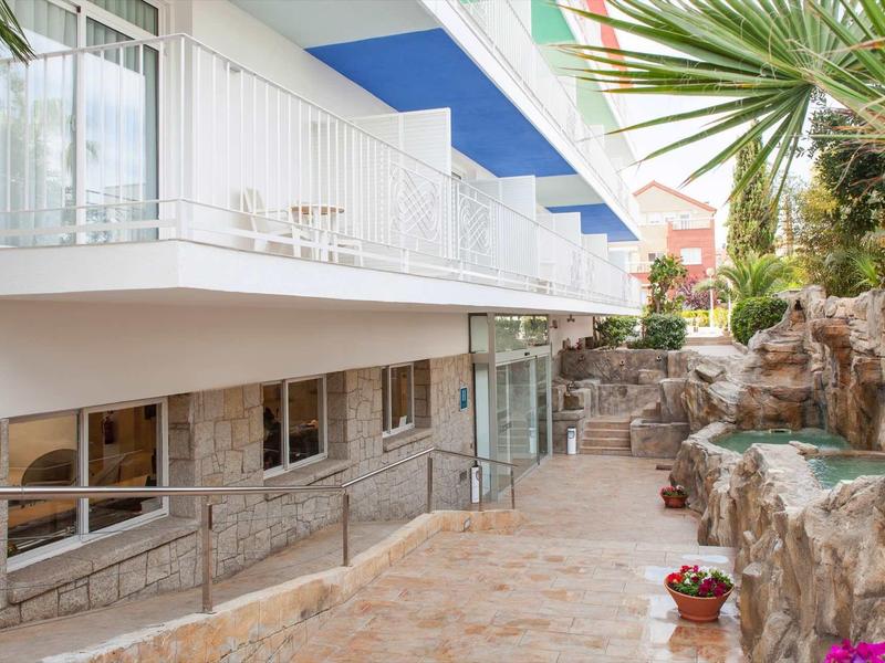 Moderner Außenbereich mit Terrasse, Felsenwand, Pflanzen und weißem mehrstöckigen Gebäude.