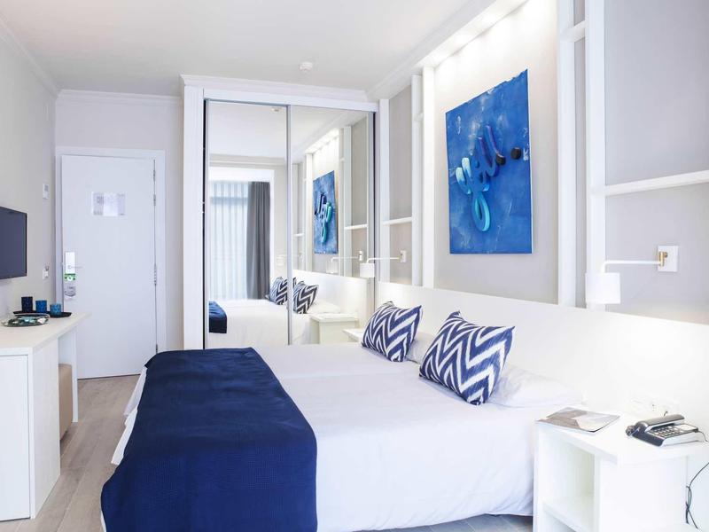 Modernes Schlafzimmer mit weißem Bett, blauen Kissen, Wandbildern und einem großen Spiegel.