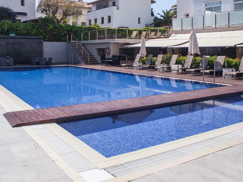 Ein blauer Außenpool mit Liegestühlen und Sonnenschirmen in einem modernen Hotelbereich.