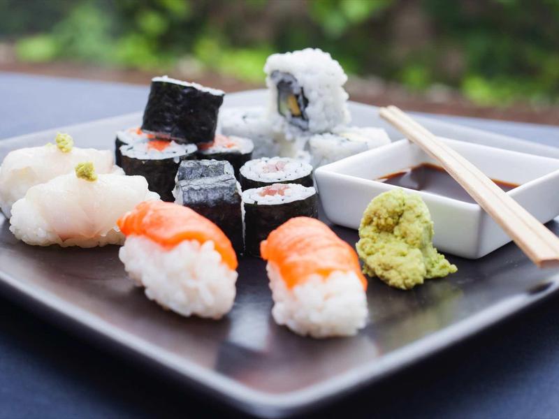 Verschiedene Sushi-Stücke mit Wasabi, Ingwer und Sojasauce auf schwarzem Teller arrangiert.