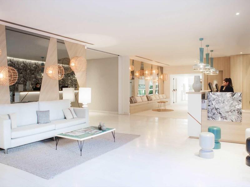 Helles, modernes Wohnzimmer mit weißem Boden, weißen Möbeln und dekorativen Pendelleuchten.