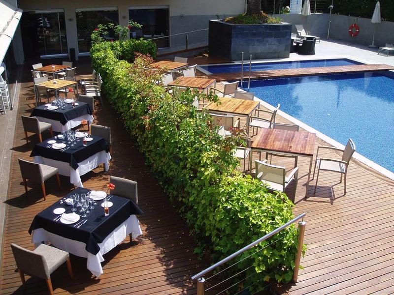 Moderner Außenbereich mit Pool, Holzboden, Tischen mit blauen Tischdecken und grünen Hecken.