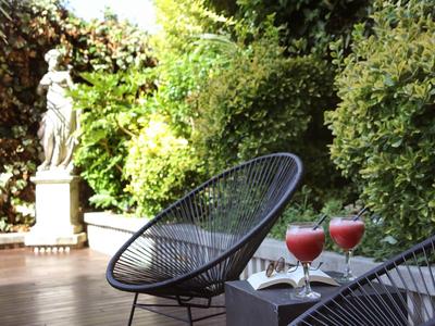 Deux cocktails sur une table à côté de chaises noires sur une terrasse avec une statue et des plantes vertes.