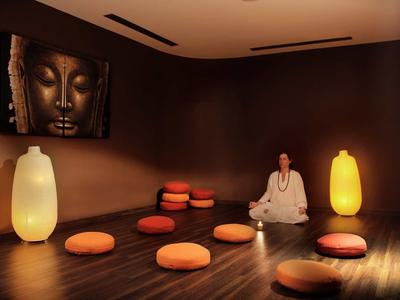 Salle de méditation conviviale avec coussins, lumière chaude et peinture de Bouddha au mur.
