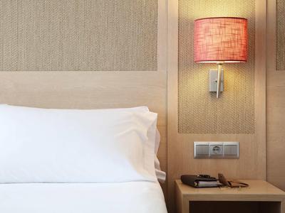 Oreiller blanc et lit avec table de chevet, abat-jour rouge et interrupteur mural.