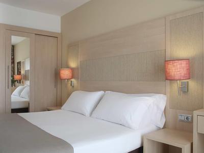 Chambre d'hôtel moderne avec grand lit double, lampes de chevet et miroir mural.