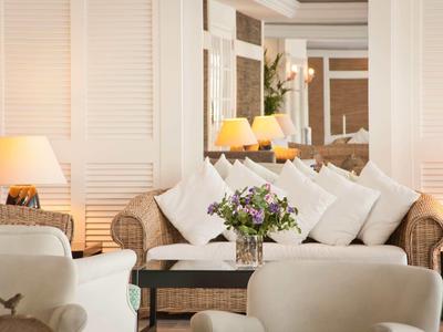 Salon d'hôtel confortable avec fauteuils en osier, coussins blancs et bouquet sur la table.