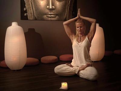 Femme médite en tenue blanche dans une pièce calme et tamisée avec image de Bouddha et lumière de bougie