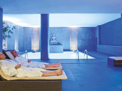 Deux personnes se détendent sur des transats à côté d'une piscine intérieure éclairée dans un spa.