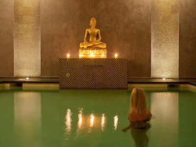 Statue de Bouddha illuminée au-dessus d'un bassin d'eau verte calme dans un temple.