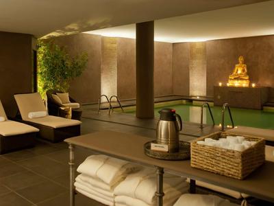 Espace spa relaxant avec piscine, chaises longues, éclairage doux et statue de Bouddha.