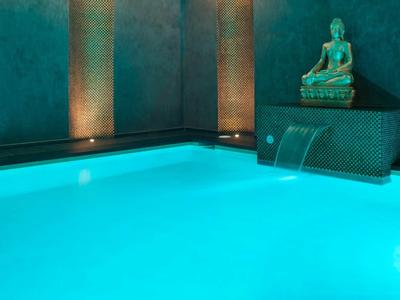 Piscine intérieure éclairée avec cascade et statue de Bouddha dans un cadre calme.