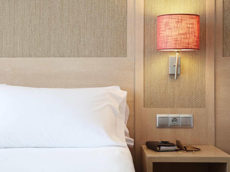 Oreiller blanc et lit avec table de chevet, abat-jour rouge et interrupteur mural.