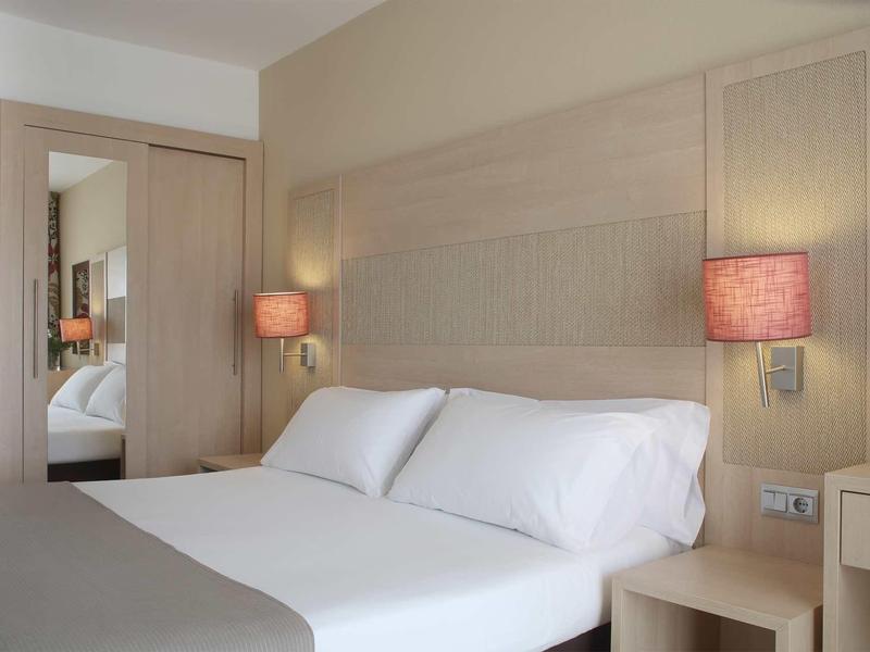 Chambre d'hôtel moderne avec grand lit double, lampes de chevet et miroir mural.