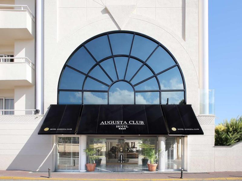 Entrée d'hôtel avec auvent noir et grande fenêtre reflétant le ciel.