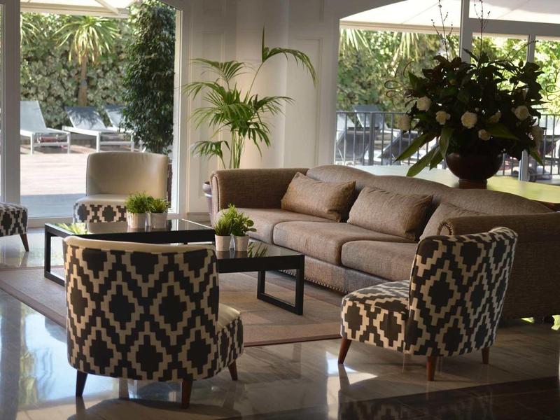 Hall d'hôtel élégant avec fauteuils, canapé et plantes vertes sous des parasols.