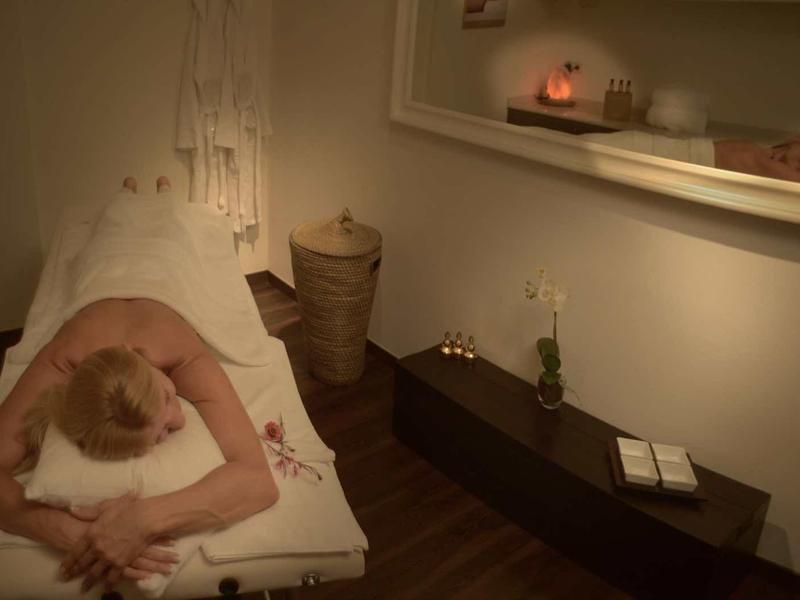 Personne détendue allongée sur une chaise longue dans une pièce de spa calme pour un massage ou un soin.