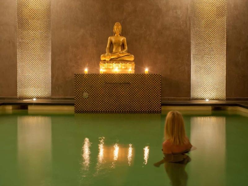 Statue de Bouddha illuminée au-dessus d'un bassin d'eau verte calme dans un temple.
