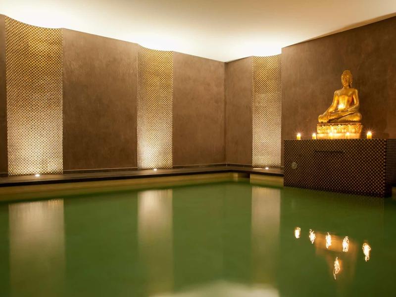 Piscine intérieure avec éclairage chaud et statue de Bouddha dans une ambiance spa relaxante.