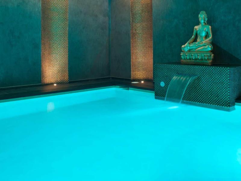 Piscine intérieure éclairée avec cascade et statue de Bouddha dans un cadre calme.