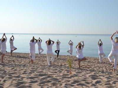 Gruppo che pratica yoga sulla spiaggia all'alba con vista sul mare calmo.