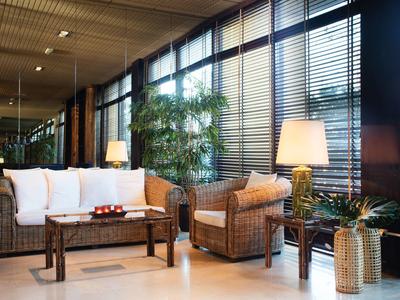 Sala de estar de hotel con muebles de mimbre, lámparas y grandes ventanas con persianas.