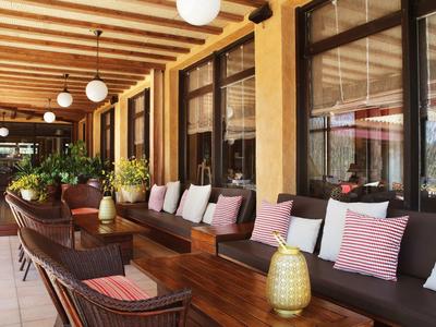 Cómodo espacio exterior con muebles de madera, cojines y plantas verdes bajo vigas de madera.