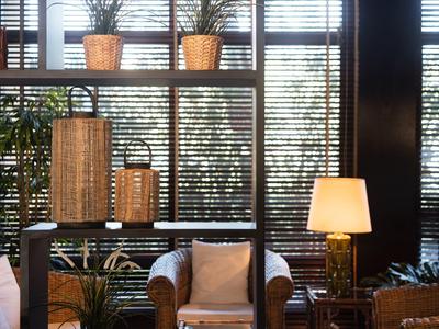 Angolo salotto accogliente con poltrone, lampade e piante, luce naturale filtrata da persiane.