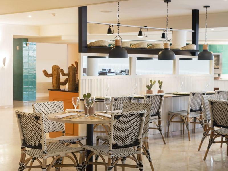 Restaurante luminoso con sillas modernas, mesas y decoración minimalista con cactus.