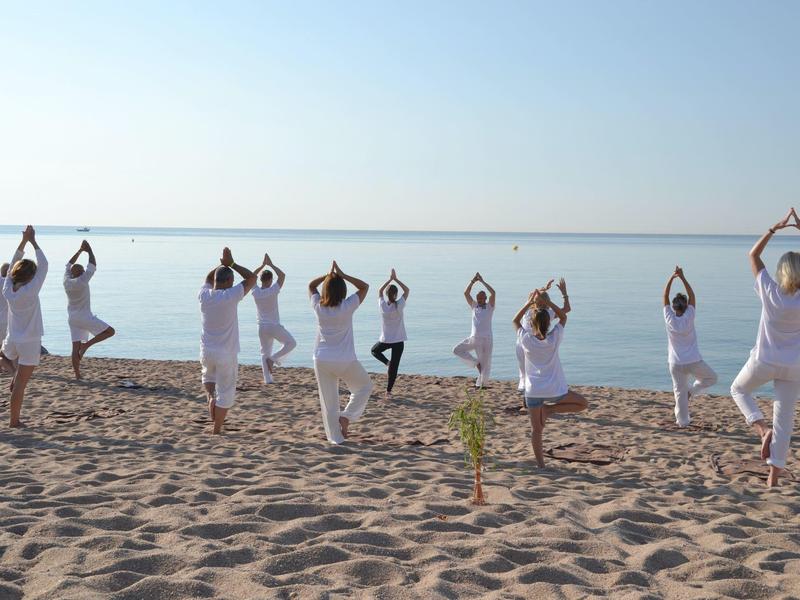 Personas practican yoga en la tranquila playa al amanecer con vista al mar.
