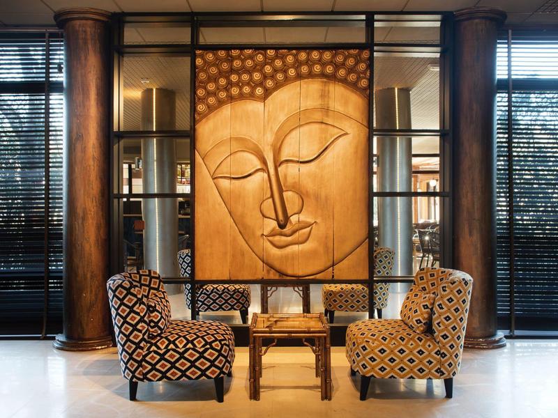 Área de descanso acogedora con sillones estampados y una gran obra de arte de Buda en la pared en un hotel.