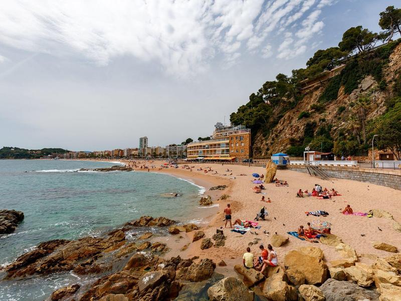 Playa con arena dorada, rocas y gente relajándose bajo un cielo nublado.